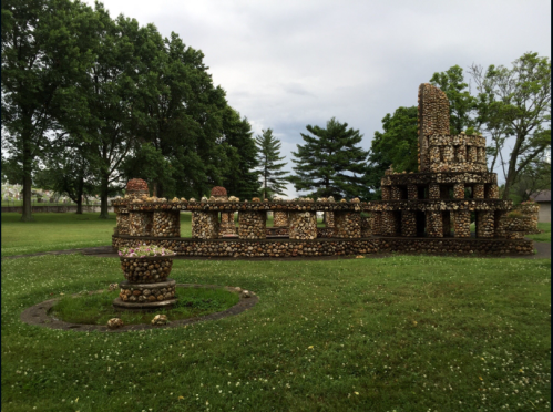 A unique stone structure resembling a small building, surrounded by trees and grassy areas under a cloudy sky.