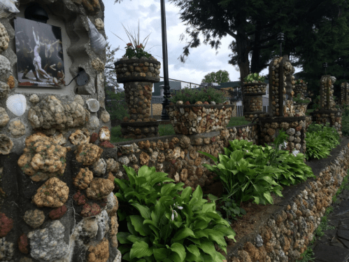 A decorative stone wall adorned with shells and plants, featuring a framed photo and lush greenery in the foreground.