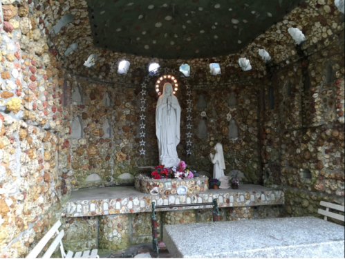 A small chapel with a statue of Mary surrounded by colorful stone walls and floral decorations.