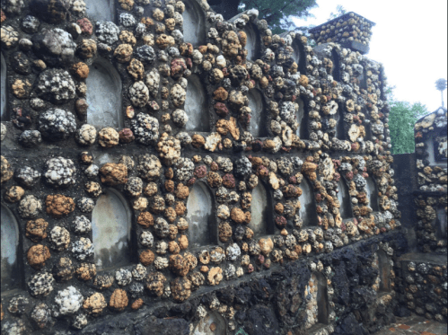 A textured wall made of colorful stones and shells, featuring arched niches and a natural, rustic appearance.