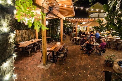 A cozy outdoor dining area with string lights, wooden tables, and patrons enjoying their meals in a lush setting.