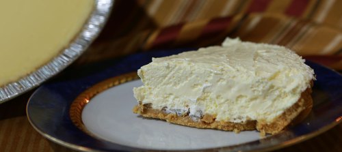 A slice of creamy cheesecake on a decorative plate, with a whole cheesecake in the background.
