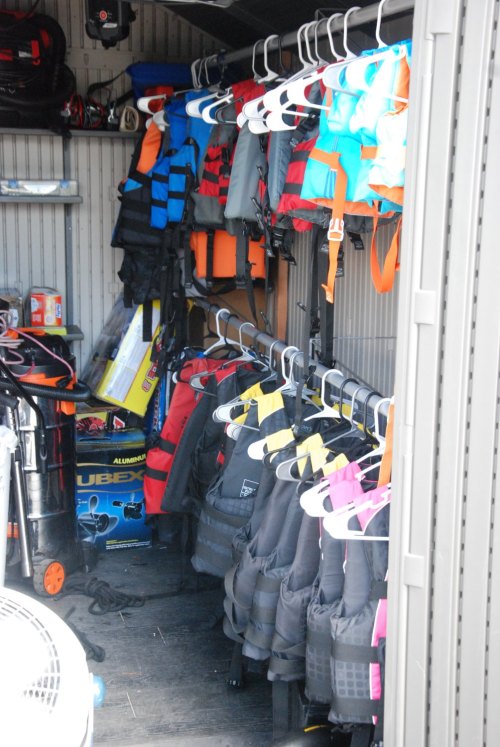 A storage area filled with colorful life jackets hanging on hooks, alongside various equipment and supplies.