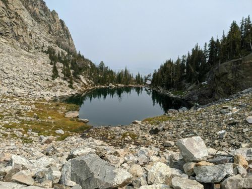A serene mountain landscape featuring a calm lake surrounded by rocky terrain and evergreen trees.