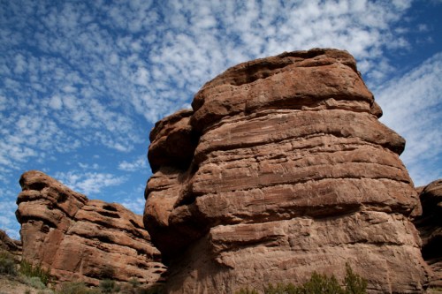 A towering rock formation against a blue sky with scattered clouds, showcasing rugged textures and natural beauty.