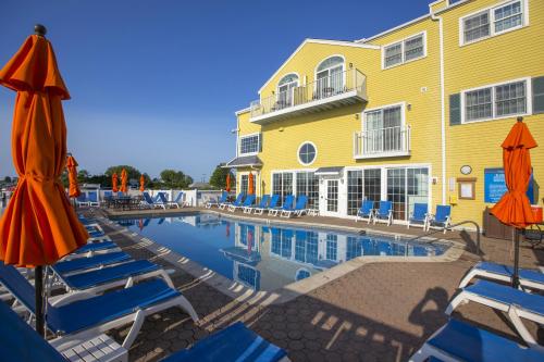 A sunny pool area with orange umbrellas, lounge chairs, and a yellow building in the background.