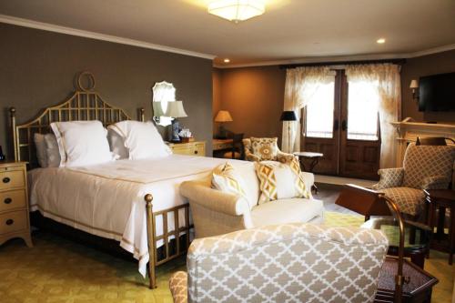 Cozy hotel room featuring a bed, armchairs, and large windows with natural light. Elegant decor and warm colors.