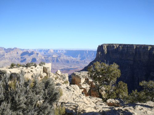 A panoramic view of the Grand Canyon, showcasing rugged cliffs and distant mesas under a clear blue sky.