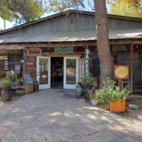 A rustic wooden building with a welcoming entrance, surrounded by greenery and signs for fudge and baked goods.