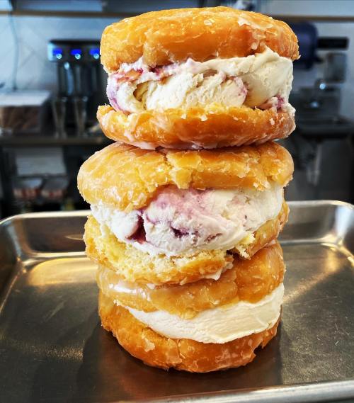 A stack of three donut sandwiches filled with ice cream and fruit swirl, resting on a metal tray.