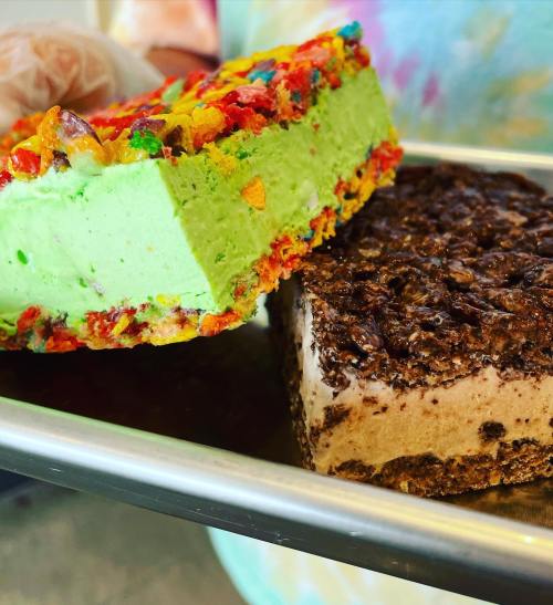 A tray holds two colorful ice cream sandwiches: one with fruity cereal and the other with a chocolatey crust.