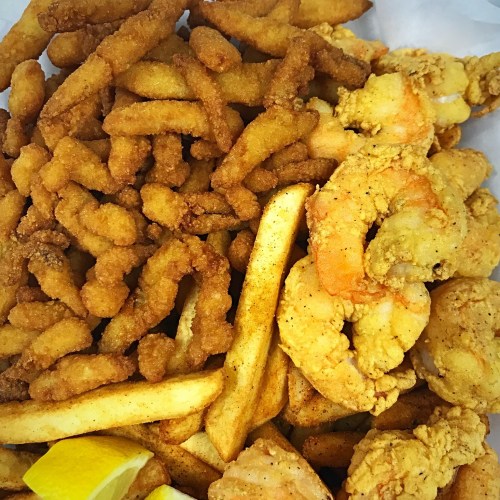 A close-up of a platter featuring golden fried shrimp, crispy fries, and crunchy fried snacks, garnished with lemon wedges.