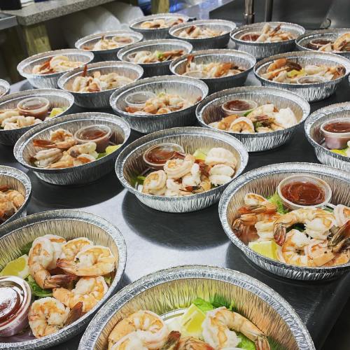 A table filled with silver bowls of shrimp, garnished with lettuce and lime, accompanied by dipping sauce.