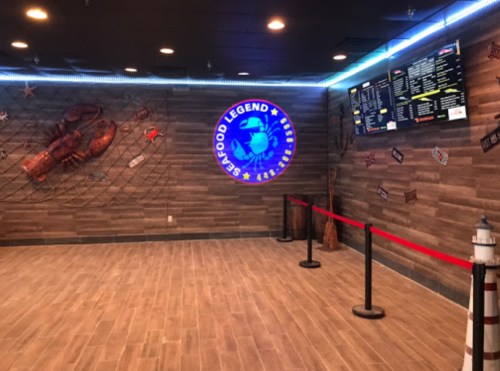 Interior of a seafood restaurant featuring a lobster sign, menu board, and a red rope barrier.