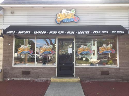 Exterior of a restaurant named "Purge's Wings & Seafood," featuring a sign and large windows displaying the menu items.