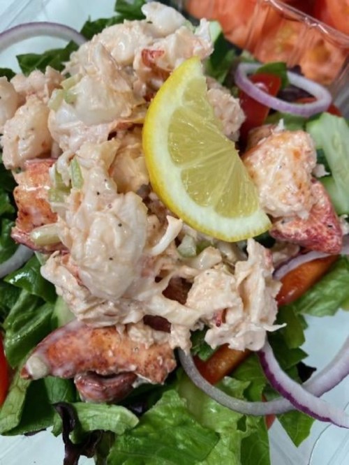 A fresh salad topped with lobster salad, garnished with a lemon slice, served on a bed of mixed greens and vegetables.