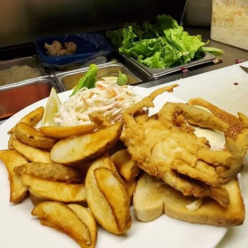 A plate of fried fish on toast, served with golden potato wedges and a side of coleslaw and lettuce.