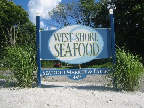 Sign for West Shore Seafood, a seafood market and eatery, featuring blue and white colors with grass in the foreground.