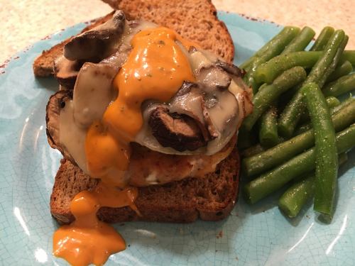 A slice of whole grain toast topped with mushrooms, melted cheese, and sauce, served with green beans on the side.