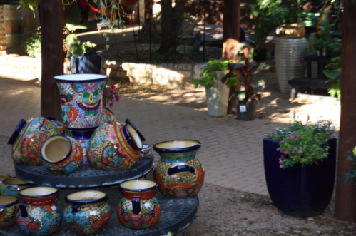 Colorful decorative pots stacked on a table in a garden setting, surrounded by greenery and other plants.