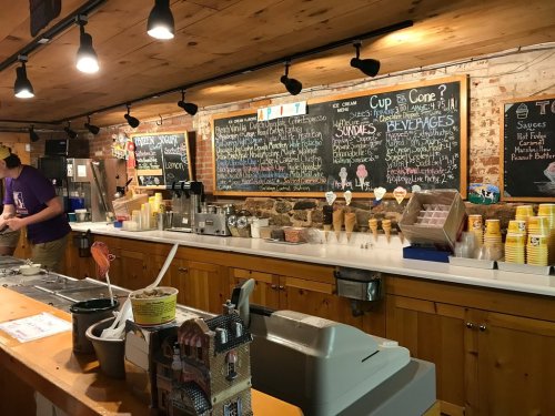 A cozy ice cream shop with a chalkboard menu, serving cones and sundaes, and a counter filled with ice cream supplies.