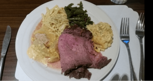 A plate of food featuring roast beef, macaroni and cheese, green beans, and a baked dish, served on a white plate.