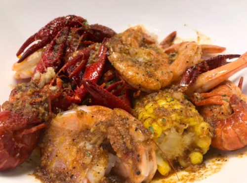A close-up of a dish featuring shrimp, crawfish, and corn, all seasoned with spices in a white bowl.
