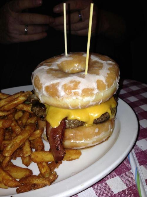 A burger stacked between two glazed donuts, topped with cheese and bacon, served with a side of fries.