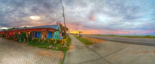 A colorful building by the roadside at sunset, with a vibrant sky and lush greenery surrounding the area.