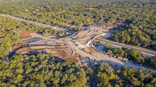 Aerial view of a construction site surrounded by trees, featuring roadwork and earthmoving activities.