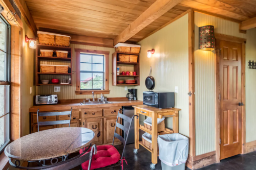 Cozy kitchen with wooden shelves, a round table, and rustic decor, featuring a sink, coffee maker, and storage baskets.