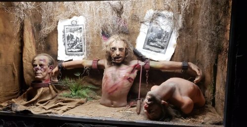 A creepy display featuring lifelike mannequins with gruesome features, set in a dark, eerie environment.