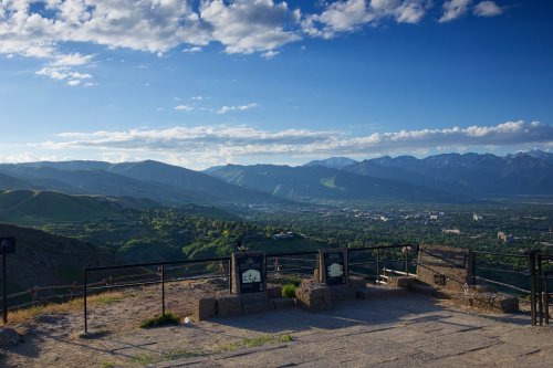 A panoramic view of mountains and valleys under a blue sky with scattered clouds, featuring a lookout point.