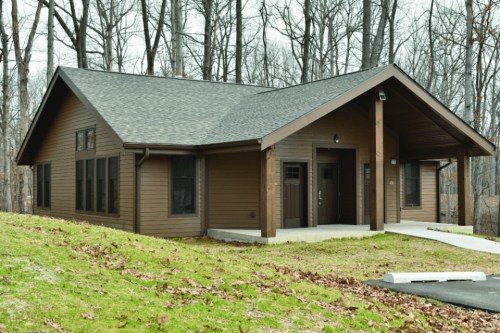 A modern brown cabin surrounded by trees, featuring a sloped roof and a welcoming entrance.