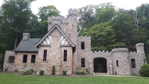 A stone castle with turrets and a green lawn, surrounded by trees in a serene outdoor setting.