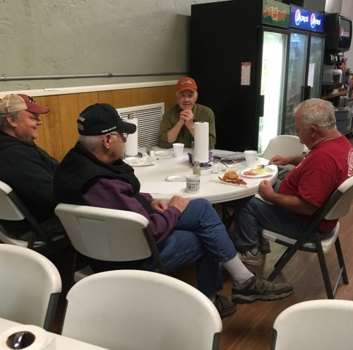 Four men sitting around a table in a casual dining setting, enjoying food and conversation.