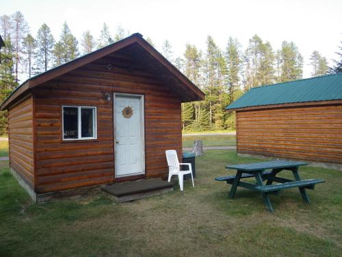 A rustic wooden cabin with a white door and a picnic table outside, surrounded by trees and grassy area.