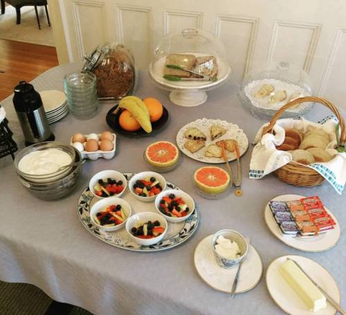 A breakfast spread featuring fruit bowls, yogurt, eggs, bread, pastries, and butter on a table.