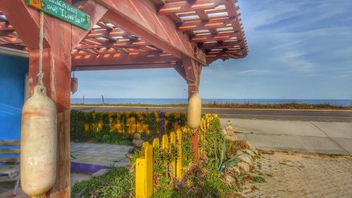 A colorful seaside view from a porch with a wooden structure, plants, and a calm ocean in the background.