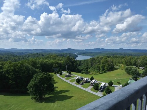 A scenic view from a high vantage point, showcasing lush green hills, a river, and a blue sky with fluffy clouds.