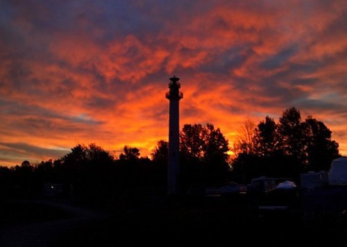 Silhouette of a tower against a vibrant sunset with colorful clouds and trees in the foreground.