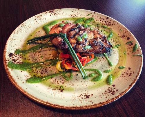A beautifully plated dish featuring grilled meat, colorful peppers, and a green sauce, garnished with chives.