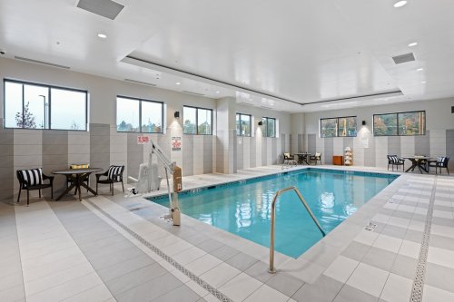 Indoor swimming pool with a lift, surrounded by windows and seating areas. Bright and modern design.