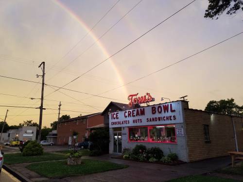 A colorful rainbow arcs over Tom's Ice Cream Bowl, a charming ice cream shop with a retro sign at sunset.