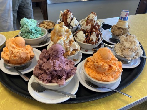 A tray of various ice cream bowls, featuring colorful scoops and toppings like nuts and caramel.