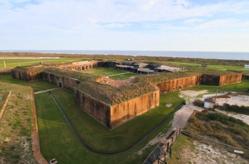 Aerial view of a historic fort surrounded by green grass and ocean, showcasing its unique star-shaped structure.