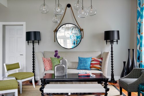 A stylish living room featuring a gray sofa, colorful pillows, a round mirror, and modern lighting fixtures.