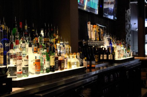 A well-stocked bar featuring various bottles of liquor and beer taps, with screens displaying sports in the background.