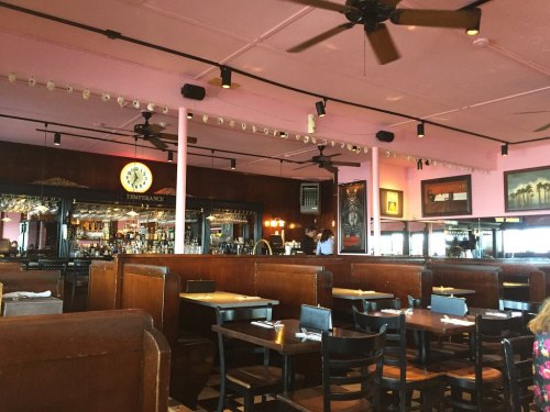 Interior of a restaurant featuring pink walls, wooden booths, a bar area, and ceiling fans.