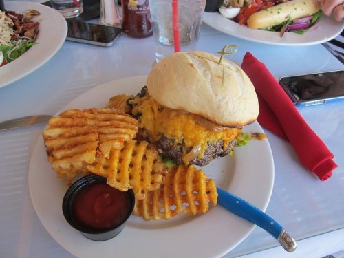 A juicy cheeseburger with melted cheese, served with waffle fries and a side of ketchup on a white plate.